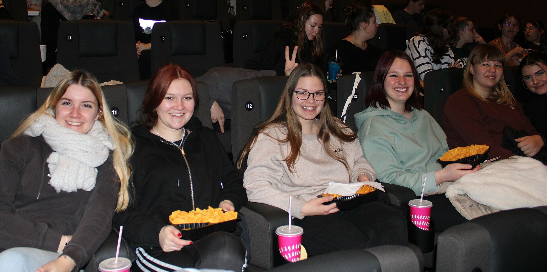 Vier Studierende mit Popcorn und Getränken im Kino. 