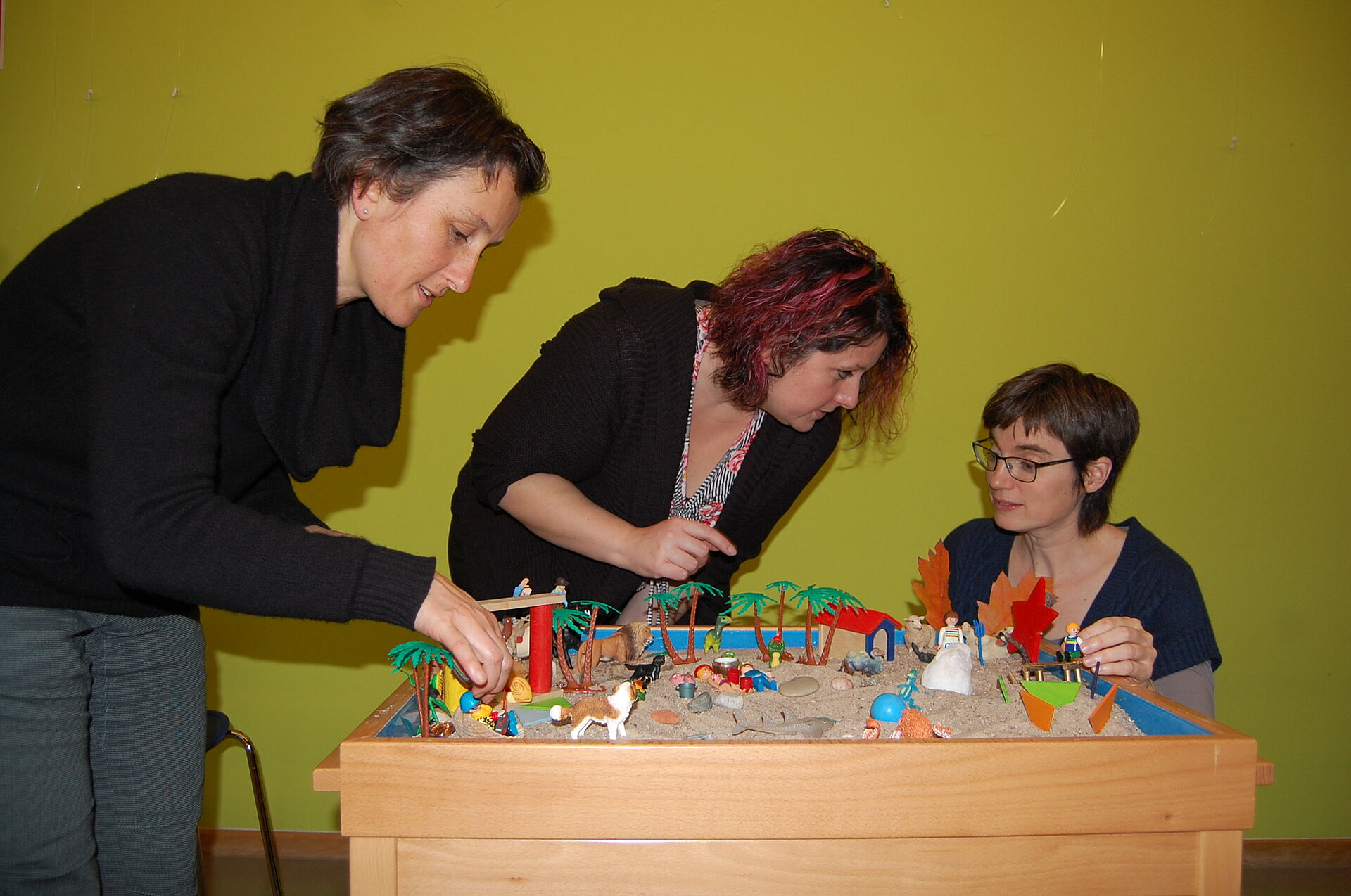 Drei Studierende der Heilpädagogik stehen um einen Spieletisch mit Figuren. 